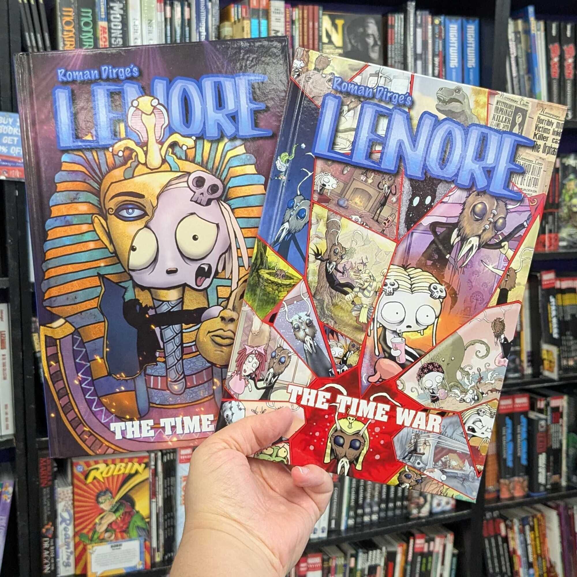 Two copies of Lenore: The Time War, each with a different cover design, held up against a wall of books in the background.