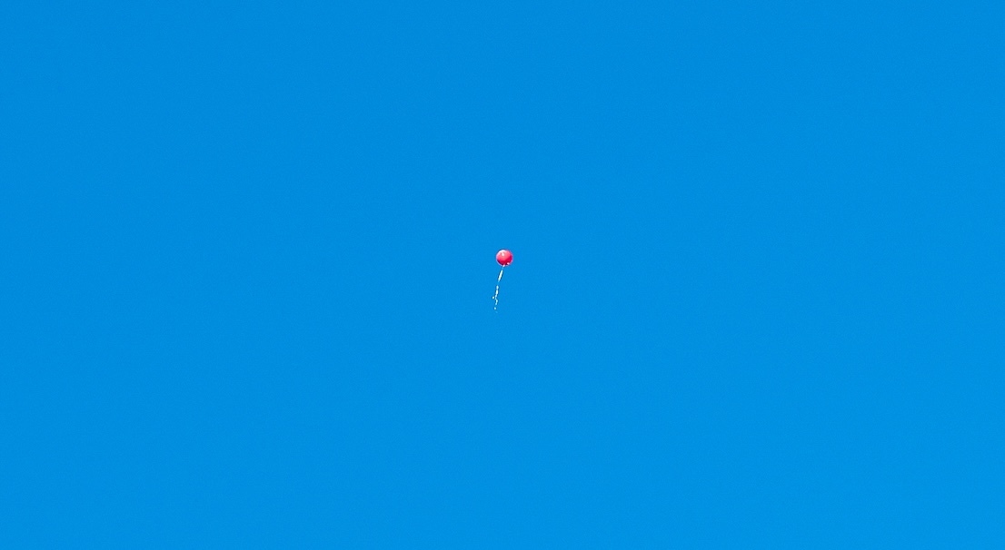 a balloon floating up into a blue sky