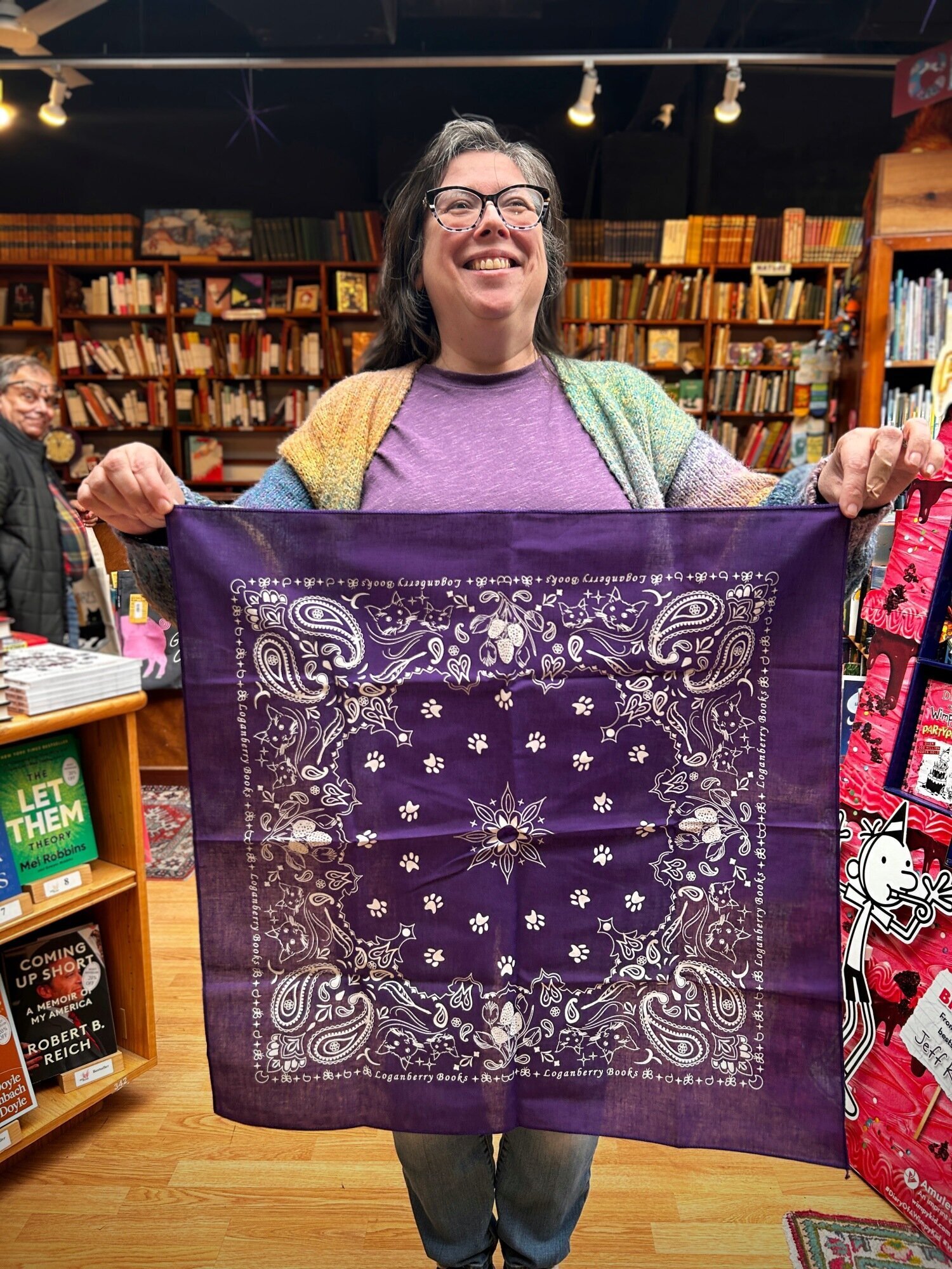 Smiling woman holds up a purple bandana with a paisley pattern for display