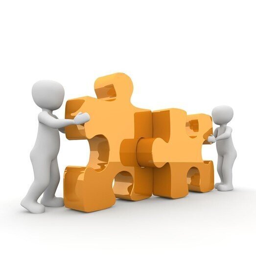 Two people pushing together two jigsaw pieces.