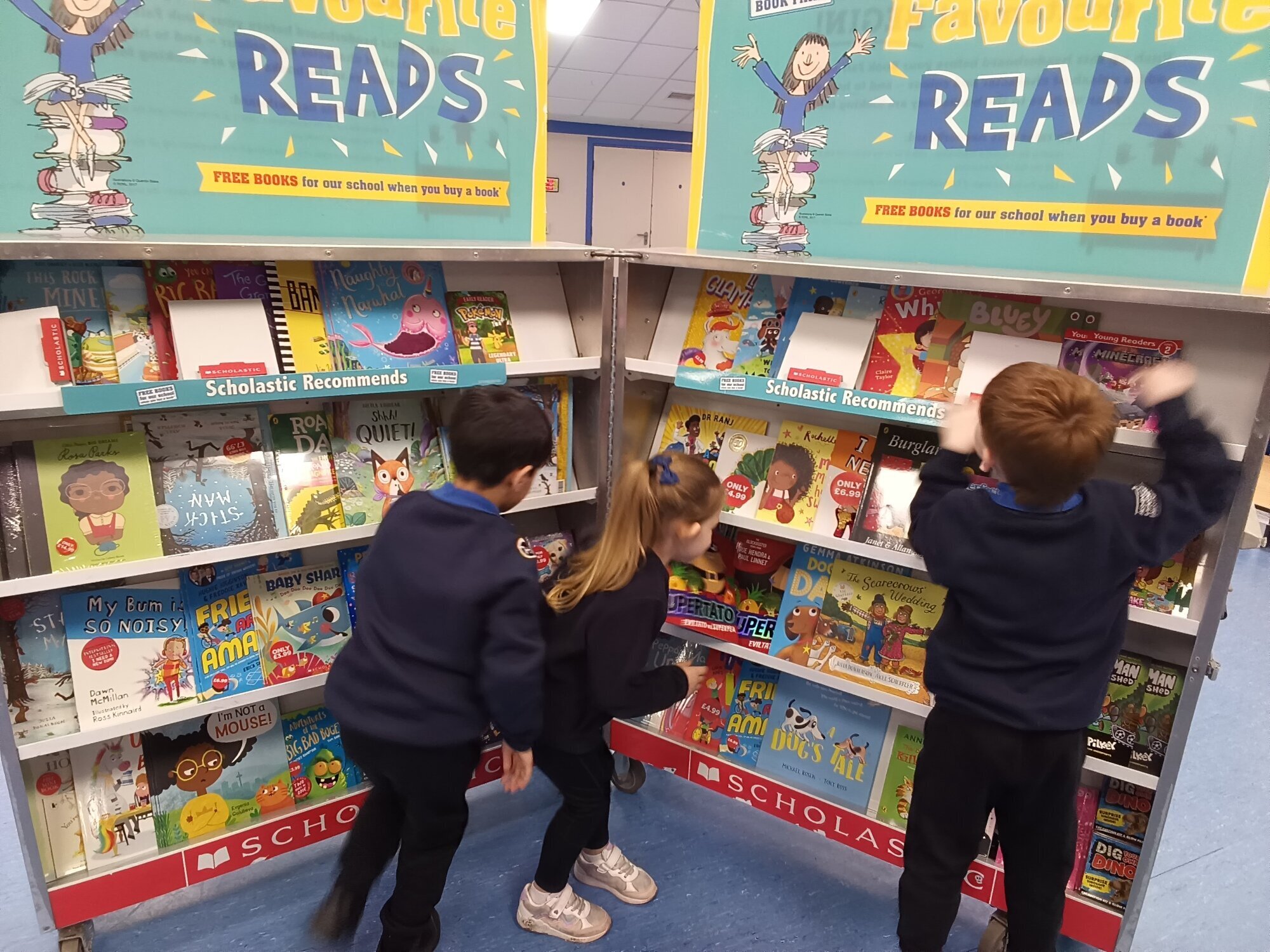 Three children excitedly choose books at the Book Fair.