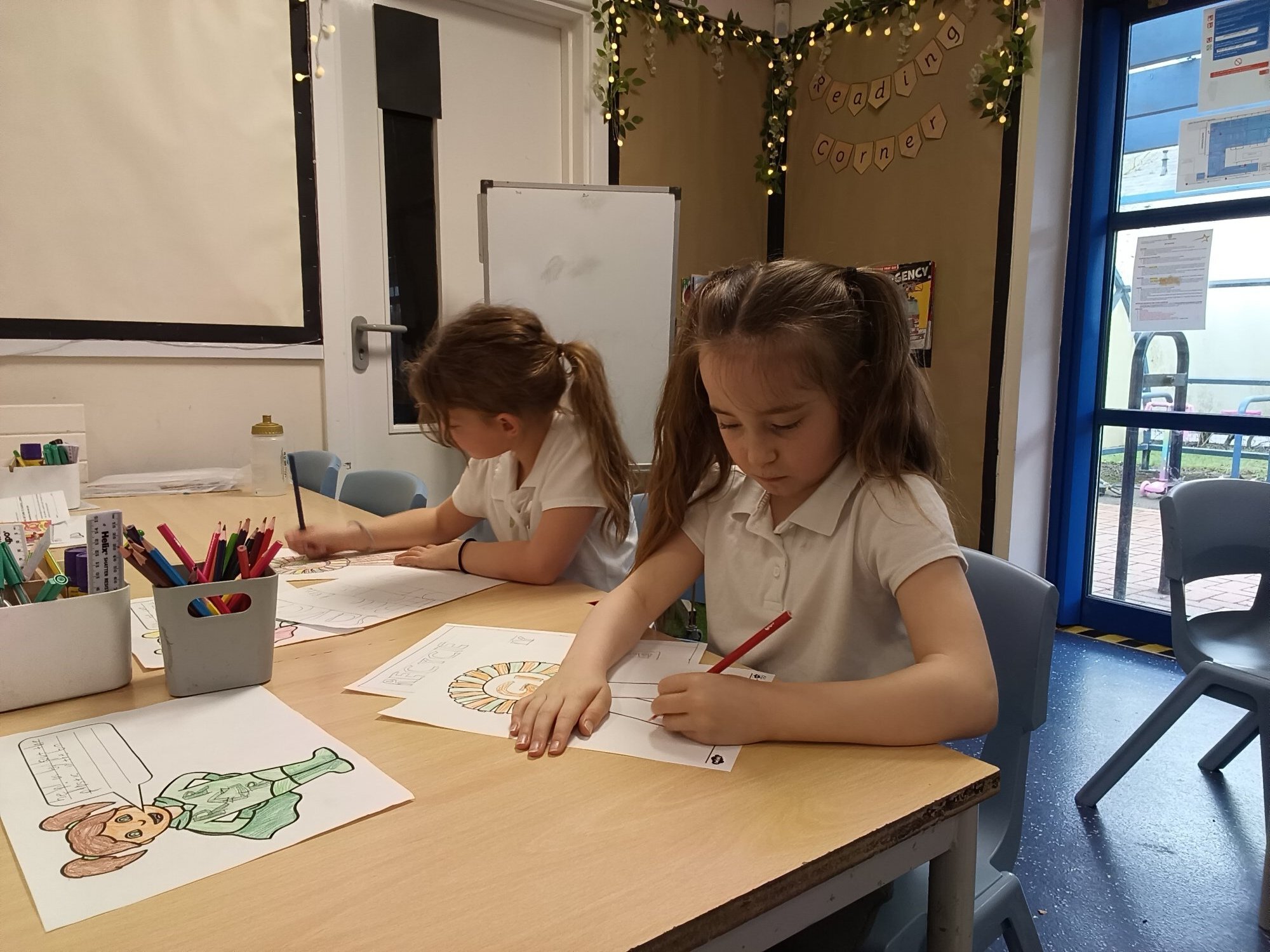 Two girls from 2NM sat at a table drawing posters for the Going Green challenge.