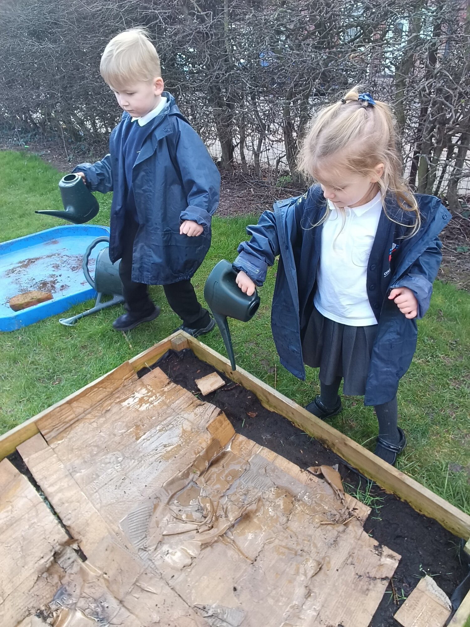 Two Reception children with watering cans in the garden.