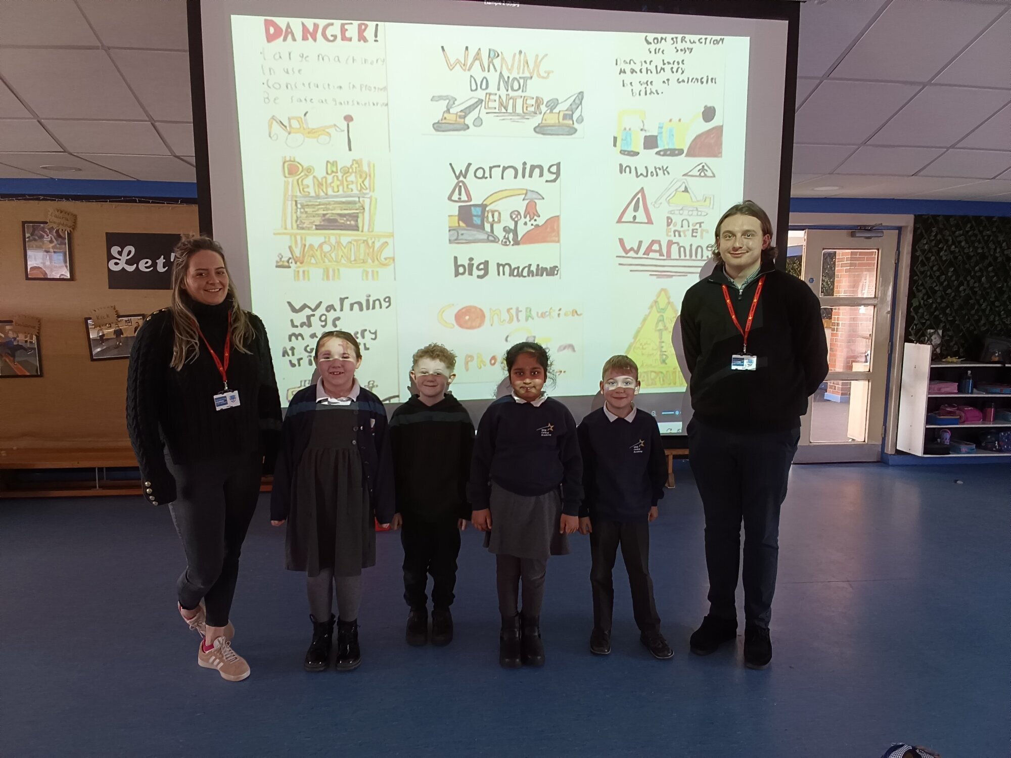 Four Year 2 children with two construction industry guests in front of a screen with safety messages
